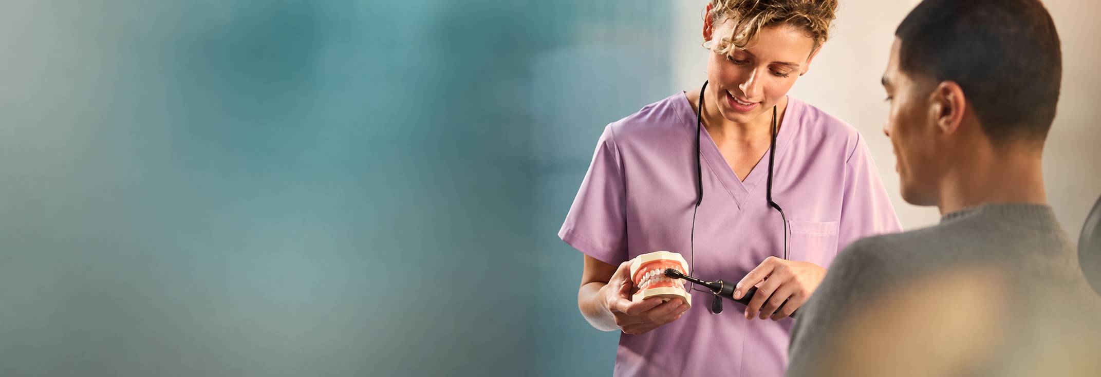 Dentální profesionálka předvádí pacientovi čištění sonickým kartáčkem